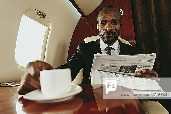 Geschäftsmann liest Zeitung mit Kaffeetasse im Flugzeug
