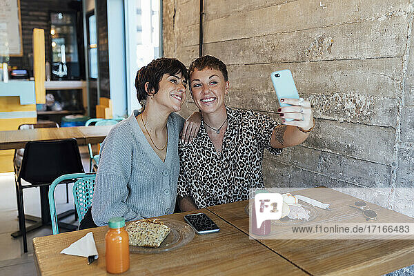 Junge Freunde lächelnd während der Aufnahme von Selfie durch Handy sitzen im Restaurant
