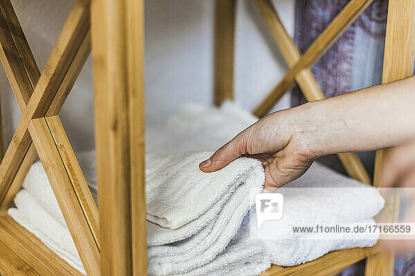 Hand einer Frau  die ein weißes Handtuch von einem Holzständer nimmt