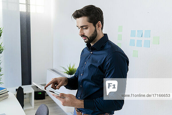 Male entrepreneur using digital tablet against wall in office