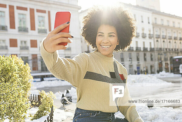 Afro woman smiling while taking selfie through mobile phone sitting in city