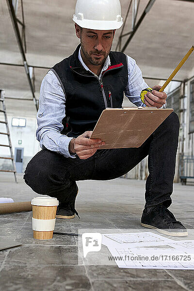 Männlicher Architekt analysiert einen Lageplan  während er in einem Gebäude auf dem Boden hockt