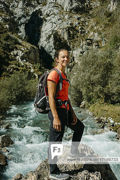 Smiling woman with backpack standing against river at Cares Trail in Picos De Europe National Park  Asturias  Spain