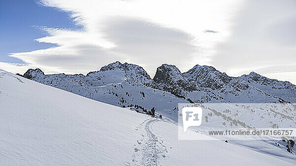 Male skier at slope of snowy mountain against cloudy sky