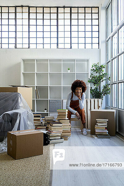 Afro-Frau mit Hand am Kinn gegen Bücherregal im neuen Zuhause