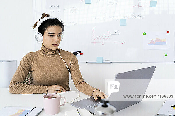 Junge Studentin beim E-Learning am Laptop über Kopfhörer zu Hause