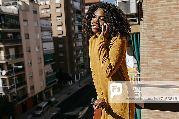 Frau mit lockigem Haar  die auf dem Balkon stehend mit ihrem Handy telefoniert