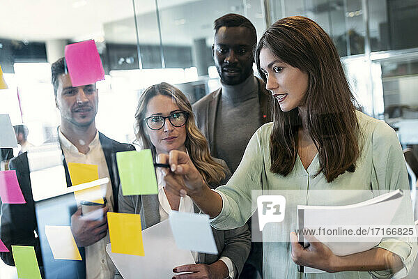 Young businesswoman explaining over adhesive note on glass wall while standing in office