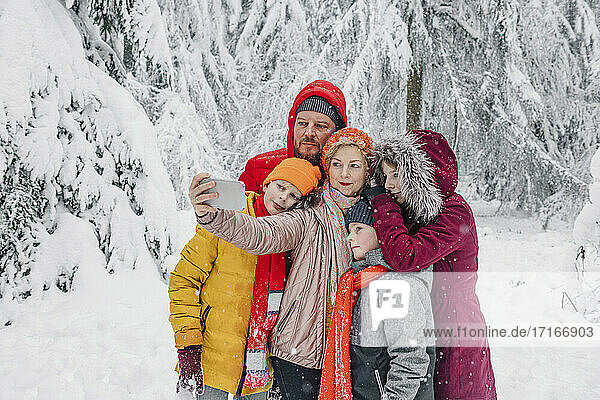 Mature woman taking selfie with family while standing in forest during snowing