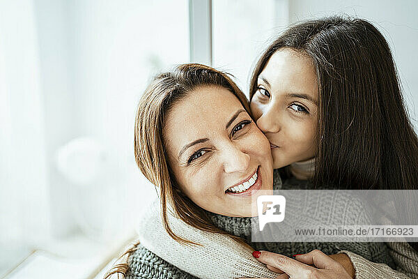 Tochter küsst glückliche Mutter am Fenster zu Hause