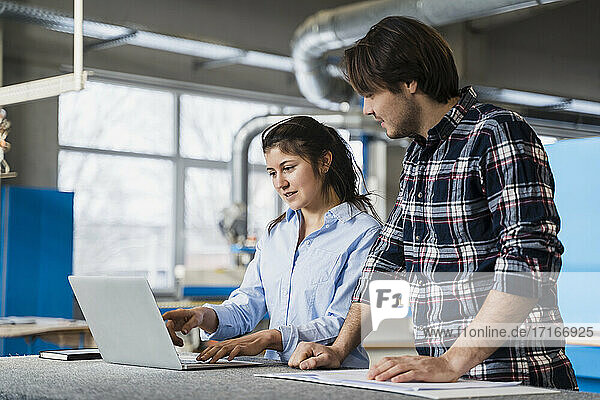 Expertise having discussion over laptop while standing by colleague at industry