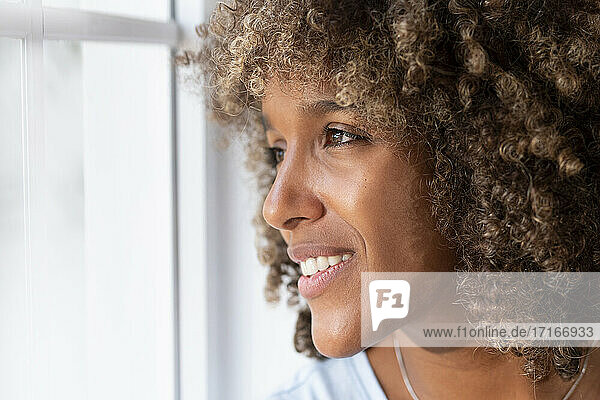 Nahaufnahme einer lächelnden Frau  die durch ein Fenster zu Hause schaut