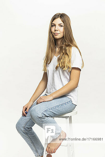 Pre-adolescent girl sitting on stool against white background in studio