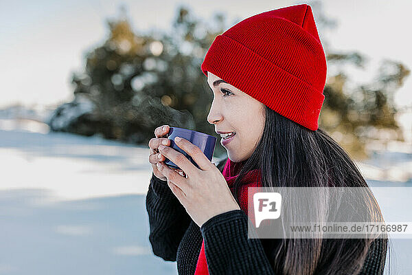 Lächelnde Frau trinkt Kaffee und genießt den Winter auf dem Lande