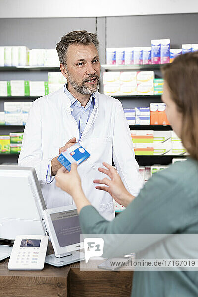 Mature pharmacist advising customer about medicine at checkout in store