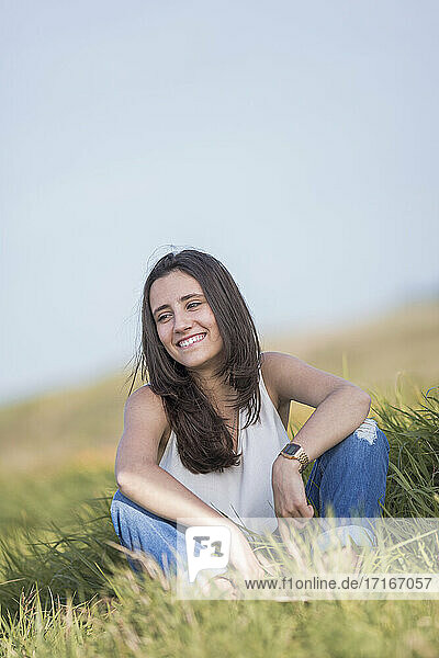 Glückliche junge Frau  die wegschaut  während sie über Gras sitzt