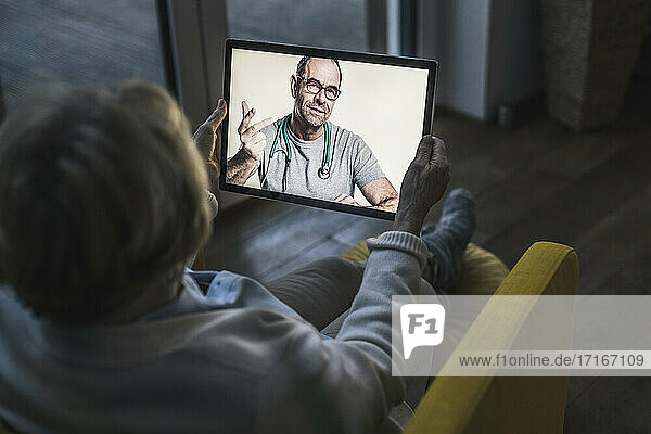 Senior patient taking advice from male doctor on video call while sitting in dark room