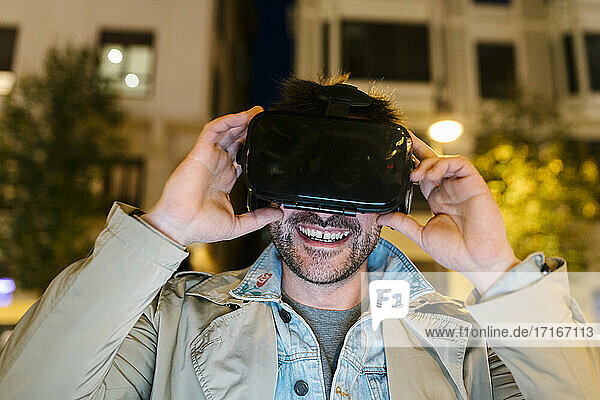 Mittelgroßer erwachsener Mann  der ein Virtual-Reality-Headset trägt  während er im Freien sitzt