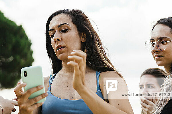 Frau schaut auf Telefon mit Freunden gegen Himmel