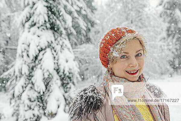 Ältere Frau lächelt im Winter im Wald stehend
