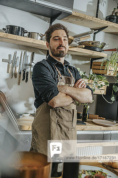 Confident male chef standing with arms crossed in kitchen