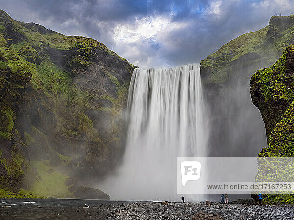 Travelers at Skogafoss waterfall against cloudy sky  Iceland