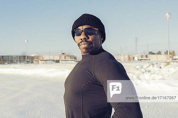 Muskulöser Sportler mit Sonnenbrille  der an einem sonnigen Tag im Schnee steht
