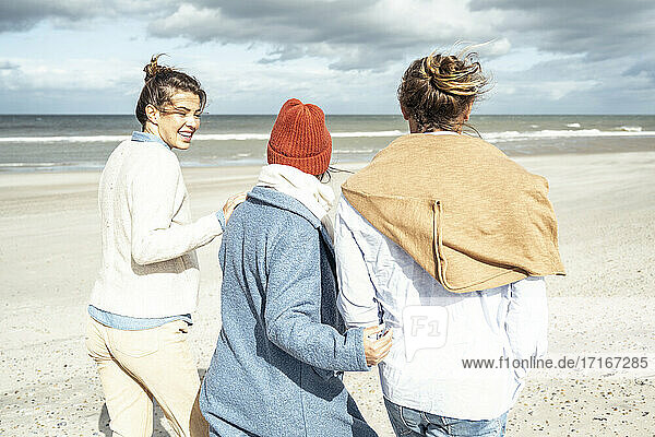 Group of friends walking together along sandy coastal beach
