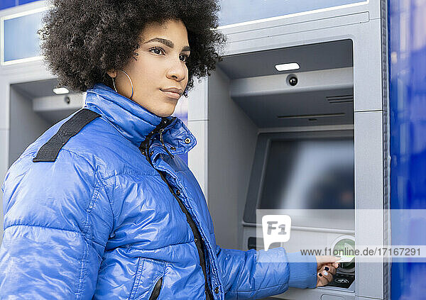 Afro woman removing ticket from ticket machine while standing bus stop