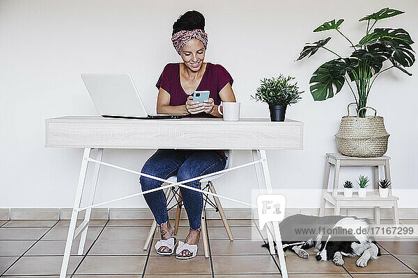 Lächelnde Unternehmerin  die ihr Smartphone an einer weißen Wand im Büro zu Hause benutzt
