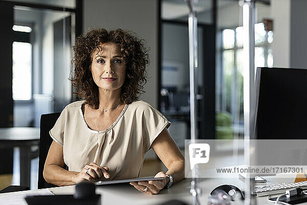 Selbstbewusste Geschäftsfrau  die ein digitales Tablet benutzt  während sie im Büro sitzt