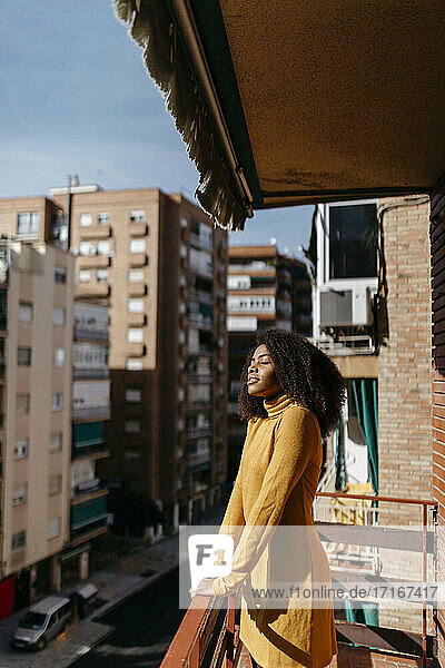 Junge Frau steht mit geschlossenen Augen auf dem Balkon