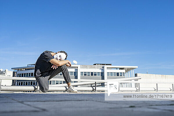 Man with white mask crouching on rooftop against sky