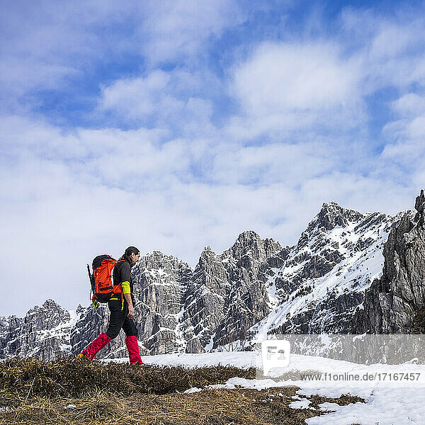 Man hiking on snowcapped mountain against cloudy sky