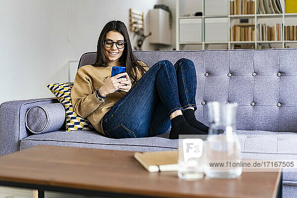 Smiling woman using mobile phone while relaxing on sofa at home