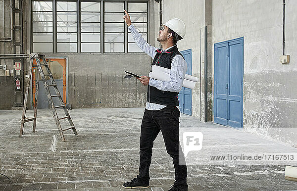 Männlicher Architekt mit digitalem Tablet  der beim Bau eines Gebäudes nach oben blickt