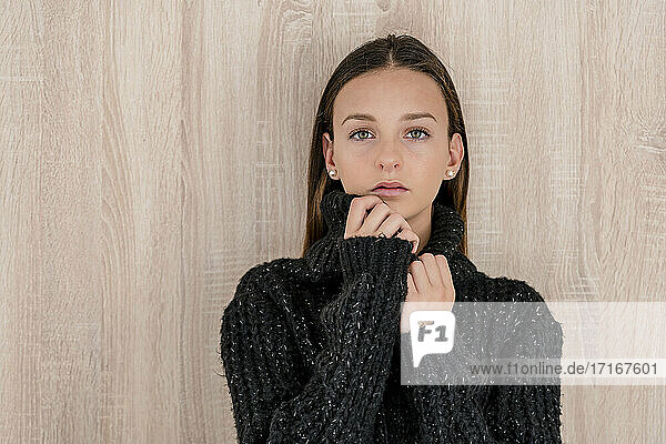 Selbstbewusstes Teenager-Mädchen in schwarzem Pullover  das zu Hause an einer Holzwand steht