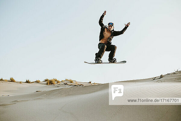 Adventurous young man jumping while sandboarding against clear sky at Almeria  Tabernas desert  Spain