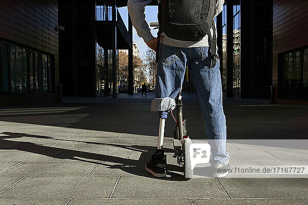 Young disabled man standing on footpath with electric push scooter in city