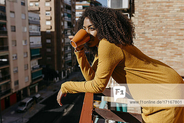 Woman drinking coffee while leaning on railing at balcony