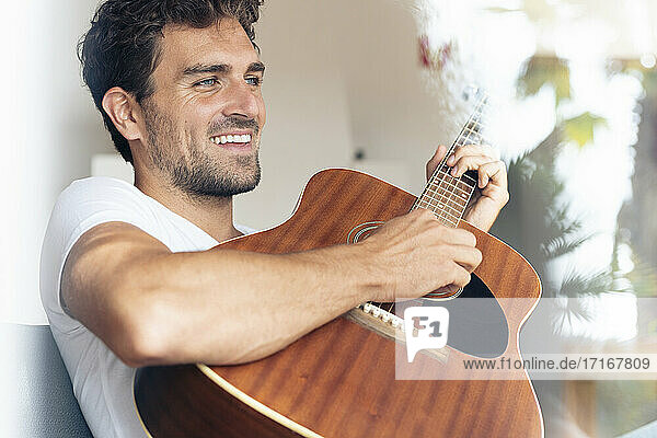Lächelnder Mann spielt Gitarre  während er zu Hause sitzt