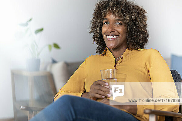 Lächelnde Frau trinkt Wasser  während sie zu Hause sitzt