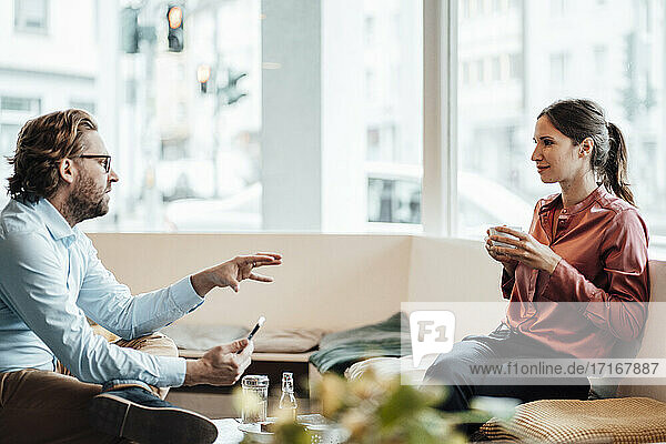 Unternehmerin trinkt Kaffee und diskutiert mit einem männlichen Kollegen in einem Café