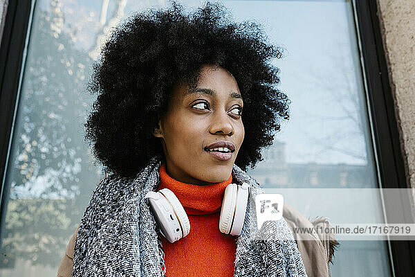 Afro-Frau mit Kopfhörern  die nachdenklich gegen eine Glaswand lehnt