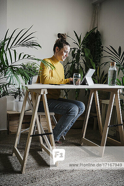 Smiling woman working on digital tablet while sitting by table at home office