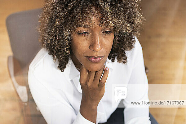 Thoughtful woman with hand on chin looking away while sitting at home