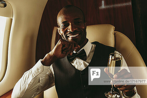 Male entrepreneur with hand on chin holding champagne in airplane