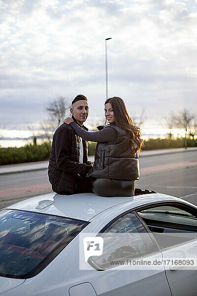 Junges Paar mit Arm um sitzen auf Autodach während Sonnenuntergang
