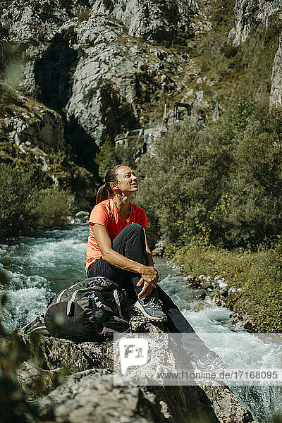 Mid adult woman looking away while sitting by river at Cares Trail in Picos De Europe National Park  Asturias  Spain