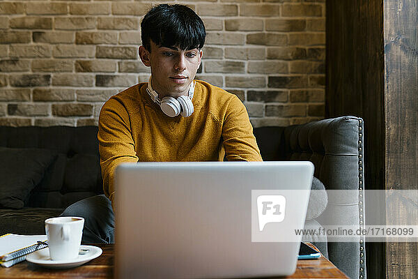 Mann mit Kopfhörern  der im Café sitzend am Laptop arbeitet